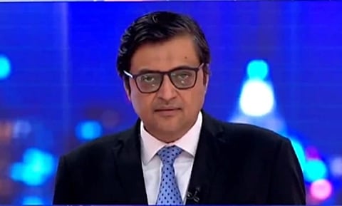 In the image Republic Bharat editor is chief Arnab Goswami is shown looking at camera with a serious face his background is blur with some blured lights and he is wearing White shirt and coat in a professional setting