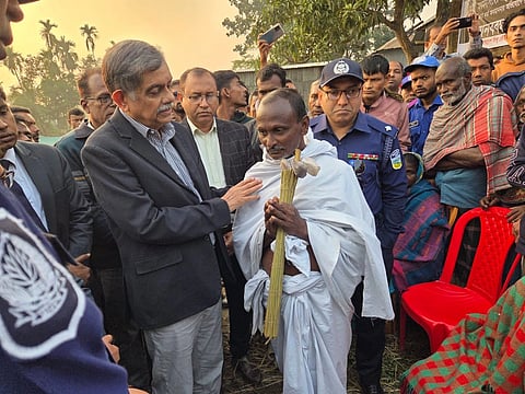 The image depicts Bangladesh Minister CR Abrar meeting and consoling Dipu Chandra Das's father. There are a lot of people in the image, Das's father is seen in a sad state wearing white dress.