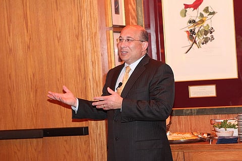 Ron Insana in a suit addressing a room. Behind him is a painting of birds, and his hands are open as if explaining something.