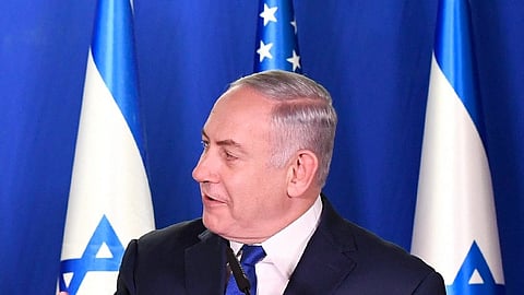 Benjamin netanyahu adressing people he is wearing a professional suit and behind him are flags of Israel