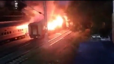 A train on a track is partially visible with a large, bright fire burning alongside it in the night, emitting intense orange and yellow flames at Andhra Pradesh on Monday.