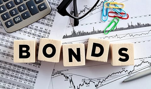 Wooden blocks spelling "BONDS" are on financial documents with charts. A calculator, glasses, and colorful paperclips create a serious and analytical tone.