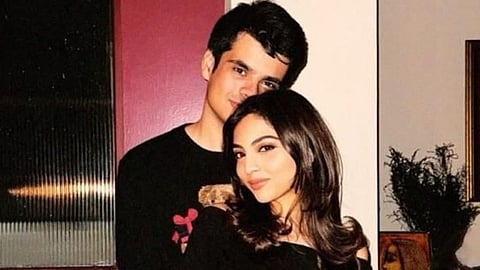 In the image Raihan Vadra and Aviva Baig are shown wearing black hugging each other behind them is a plant is shown and the setting looks like a house