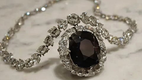 Elegant diamond necklace featuring a large dark gemstone centerpiece, surrounded by intricate silver floral accents, on a light marble surface.