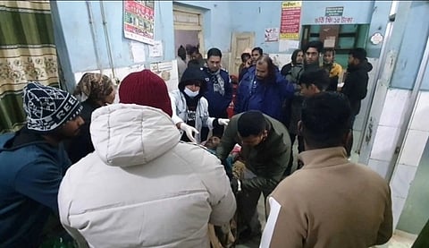 The image shows the victim, Khokon Chandra Das lying at a bed, surrounded by people, including doctors and family, in a hospital.