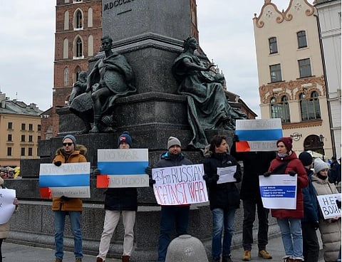 People standing together in a city square, holding signs with messages against war. The atmosphere is calm and focused on peaceful protest. image is of Russian diaspora protesting against war in Ukraine