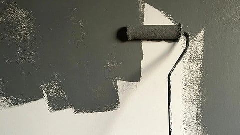 Person Holding Paint Roller While Painting the Wall, the painting process is underway