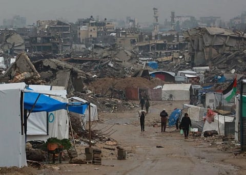 A refugee camp in Gaza, made from tents and clothes, while buildings in the background is destroyed.