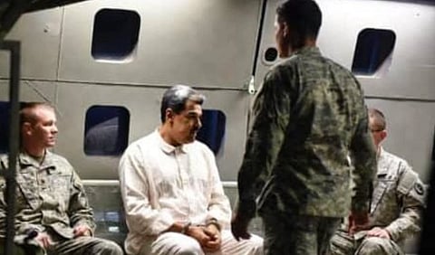 Three men in military uniforms sit inside an aircraft with a man in white attire. One soldier stands in front of the man in white, creating a tense atmosphere.