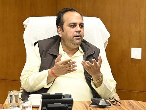 Delhi Minister Pankaj Kumar Singh addresses a press briefing . He is sitting in a chair, looking to his left and open hands.