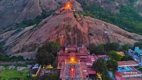 A vibrant aerial view of the Devasthanam temple complex at sunset, nestled against the large rocky Thiruparankundram hill.