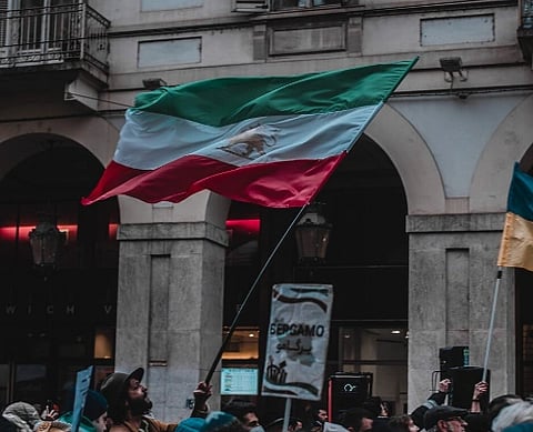 The lion and sun flag of Iran, being waved in the sky by an Iranian in the middle of the a protest ralley.