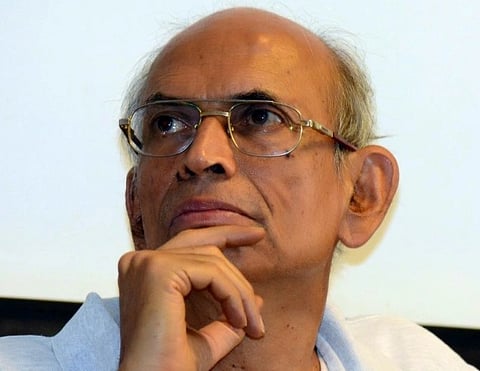 Image of veteran ecologist Madhav Gadgil with glasses he is wearing a white polo shirt, rests his chin on his hand, gazing upward.
