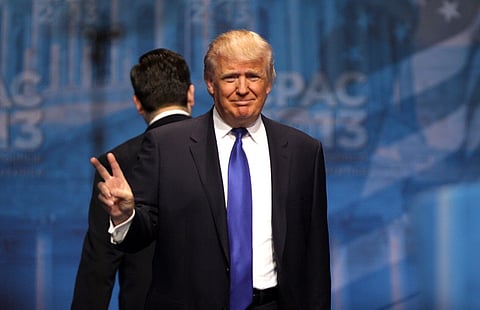 Image of Trump showing peace sign. the background of the image is blue with a light text visible. he is speaking at the 2013 Conservative Political Action Conference (CPAC) in National Harbor, Maryland.