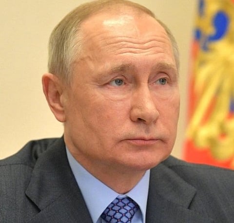 Image of Vladimir Putin in April 2020 looking towards his left. he is wearing a grey suit with dark blue stripped tie.