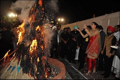 People celebrating Lohri, to the left is a bonfire and people are celebrating around it.
