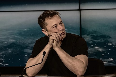 Elon Musk looking towards his left with both his hands placed on his chin. He is at the SpaceX Falcon Heavy Flight 1 post launch press conference.