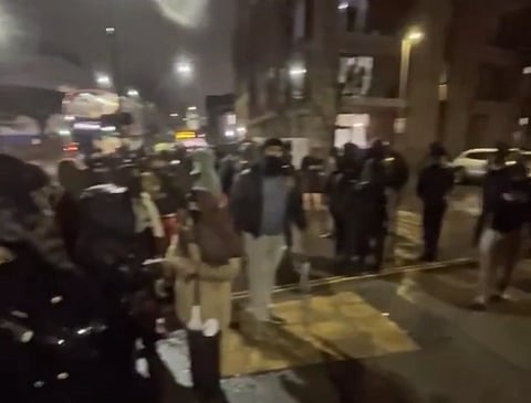 A group of people standing on a dimly lit street at night, wearing winter clothing.