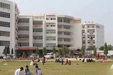 Al Galah Hospital building, people sitting on the ground covered by grass nearby