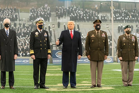 Trump stands in between Navy and Army officials on a football field, giving a thumbs up.