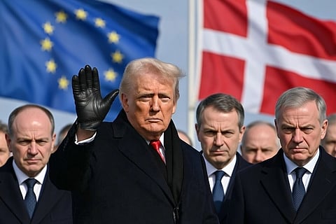 Trump in black coat and gloves, waving, while EU leaders stare at him angrily. EU and Denmark flags in the background.