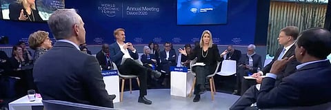 A panel of diverse individuals engages in discussion at the World Economic Forum Annual Meeting 2026. Seated on stage, they converse intently, with an audience in the background, conveying a serious and thoughtful tone.
