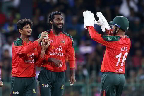 Three Bangladesh cricket players in red uniforms celebrate a successful play on the field. They display expressions of joy and camaraderie.