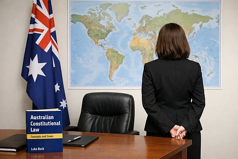 A woman (lawyer) in a black suit, back turned, stands before a world map. An Australian flag and a law book are on a desk, implying a professional setting.
