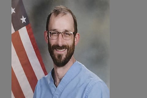 A portrait of Alex Pretti, smiling, a US flag in the background