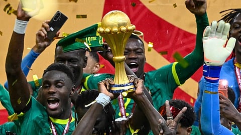 Football team in green jerseys jubilantly celebrates, lifting a golden trophy amidst falling confetti. The emotion is triumphant and joyous.