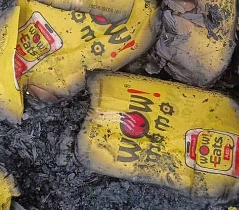 Yellow food packages labeled "Wow! Eats" are partially burned and covered in ash, suggesting a fire or destruction. The scene feels damaged and chaotic.