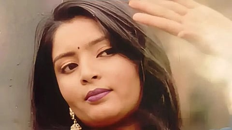 A woman named with long dark hair and gold earrings looks thoughtfully into the distance, her hand raised near her face. The mood is calm and reflective.