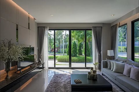 A modern, elegant living room with large sliding glass doors allowing natural light. Features a gray sofa, coffee table, and soft lighting, conveying a serene mood.