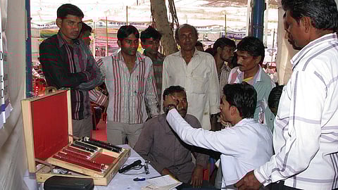 A doctor checks the eye of a patient while others crowd around at a free eye check up camp.