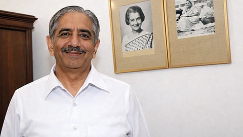 In the image RK Dhawan is shown smiling at the camera behind him are two frames of Indira Gandhi