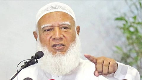Bangladesh’s Jamaat-e-Islami Chief Shafiq Rehman with a white beard and traditional cap speaking passionately at a microphone. He points with a firm expression, conveying authority.