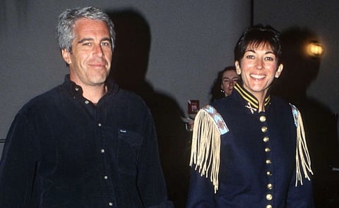 Image of Jeffrey Epstein and his then girlfriend Ghislaine Maxwell. the image is taken in a dimly lit room giving a shadowy effect. Both are looking towards the camera and smiling.