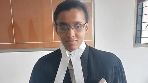 Thanya Nathan wearing a black lawyer's robe and white bands holds a thick stack of papers, standing confidently with slight smile in an office setting.