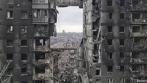 A devastated urban landscape showing heavily damaged buildings with large sections missing. The scene conveys destruction and a somber, desolate tone.