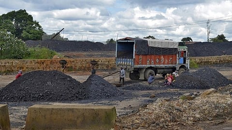 A group of workers shovel coal into large piles beside a colorful truck under a cloudy sky, conveying a scene of labor and industry in a rural area.