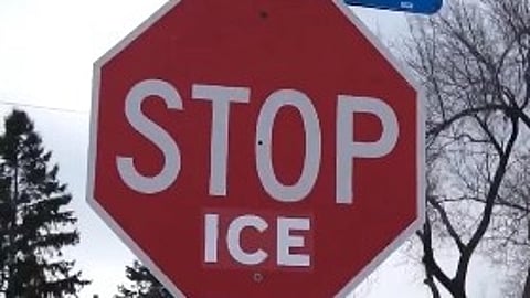 Red octagonal sign reads "STOP ICE" in bold white letters. Background has bare trees and cloudy sky, conveying a cold, winter atmosphere.