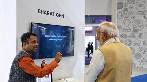 A man in an orange shirt presents information on artificial intelligence to an older man in a beige vest. The display reads "Bharat Gen" and "AI for every citizen." The setting is a technology exhibition, conveying innovation and engagement.