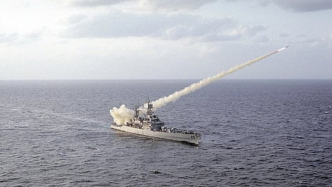 A naval ship on open waters fires a missile, trailing smoke diagonally into the cloudy sky, conveying action and military power.