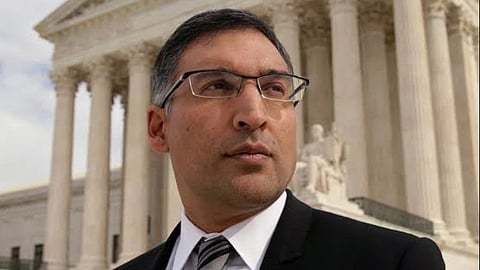 Indian-American lawyer Neal Katyal in a suit stands in front of a neoclassical building with large columns, looking determined. The sky is overcast, conveying a serious tone.