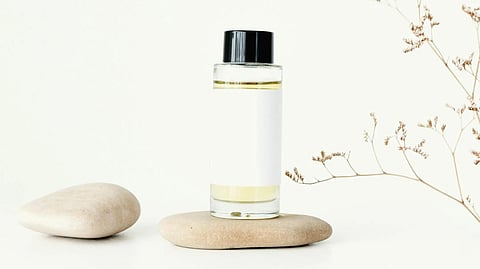 Minimalist image of a perfume bottle with a black cap on a smooth stone. Dried plant branch on right. Clean, serene, and natural ambiance.