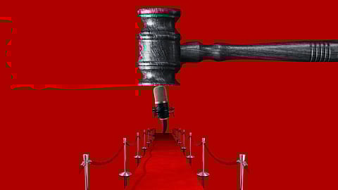 A large judge's gavel looms over a microphone on a red carpet, lined with stanchions and ropes. The image conveys a sense of judgment or decision.