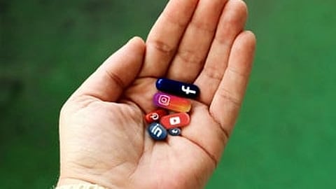 A hand holding multiple pills with different social media logos