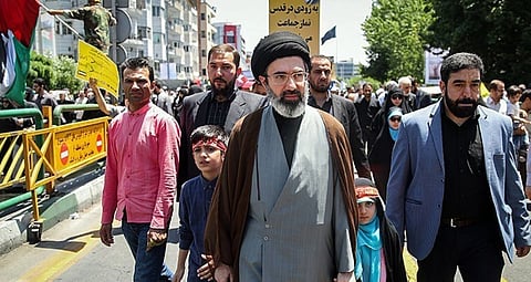 Image of Mojtaba Khamenei (center) and his children in Quds Day. A huge crowd is walking behind him with placards and flags.