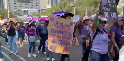 A group of people marches in a lively protest, holding signs and wearing purple clothing. The mood is energetic and focused on advocacy.