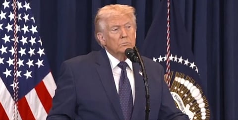 Image of Donald trump in a press conference. he is standing in front of blue curtains and American flag.